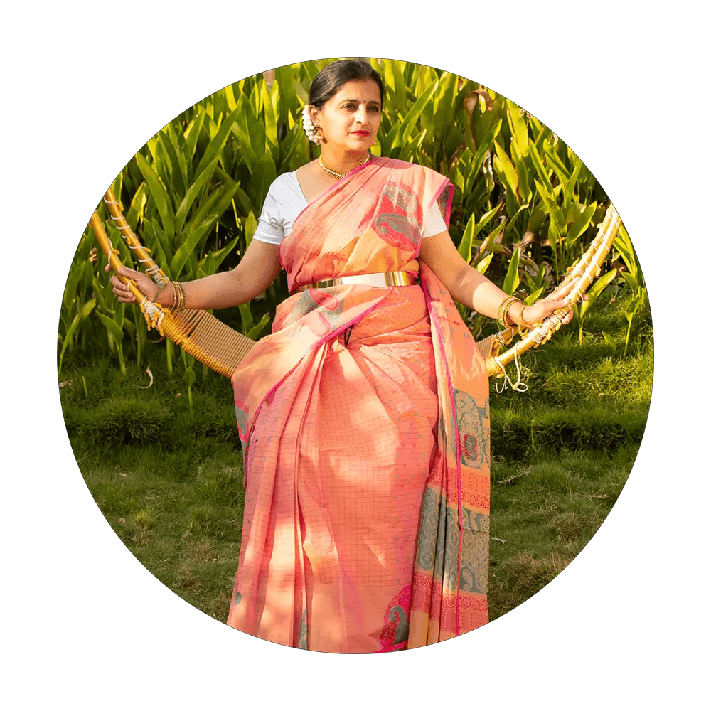 A female model sitting on a swing in a garden wearing a peach color saree from Poetic Traditions collection of Seven Sarees.