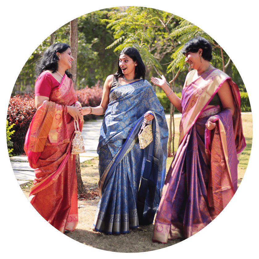 Three models laughing and chatting in a garden wearing art silk sarees from the Wedding Besties collection of Seven Sarees.
