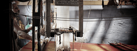 A weaver sitting in a dark room working on a handloom weaving a silk saree for seven sarees.